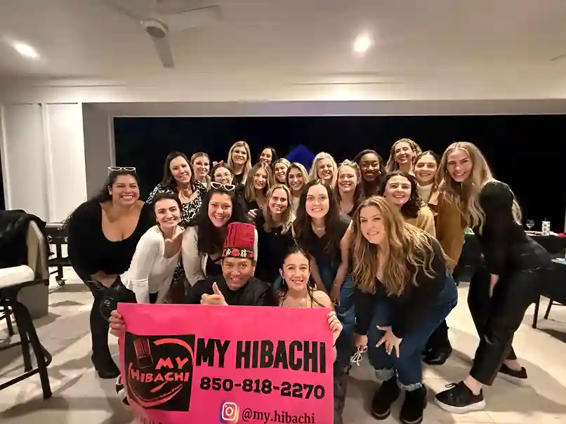 Group of women posing with My Hibachi chef holding a pink banner at indoor event