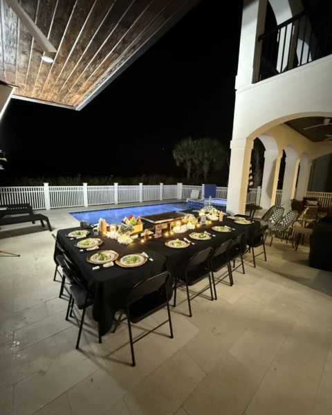 Outdoor hibachi dinner setup by the pool with black tablecloths and elegant lighting at night