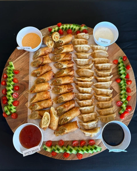 Appetizer platter with egg rolls, dumplings, sauces, and veggies at MyHibachiAtHome event
