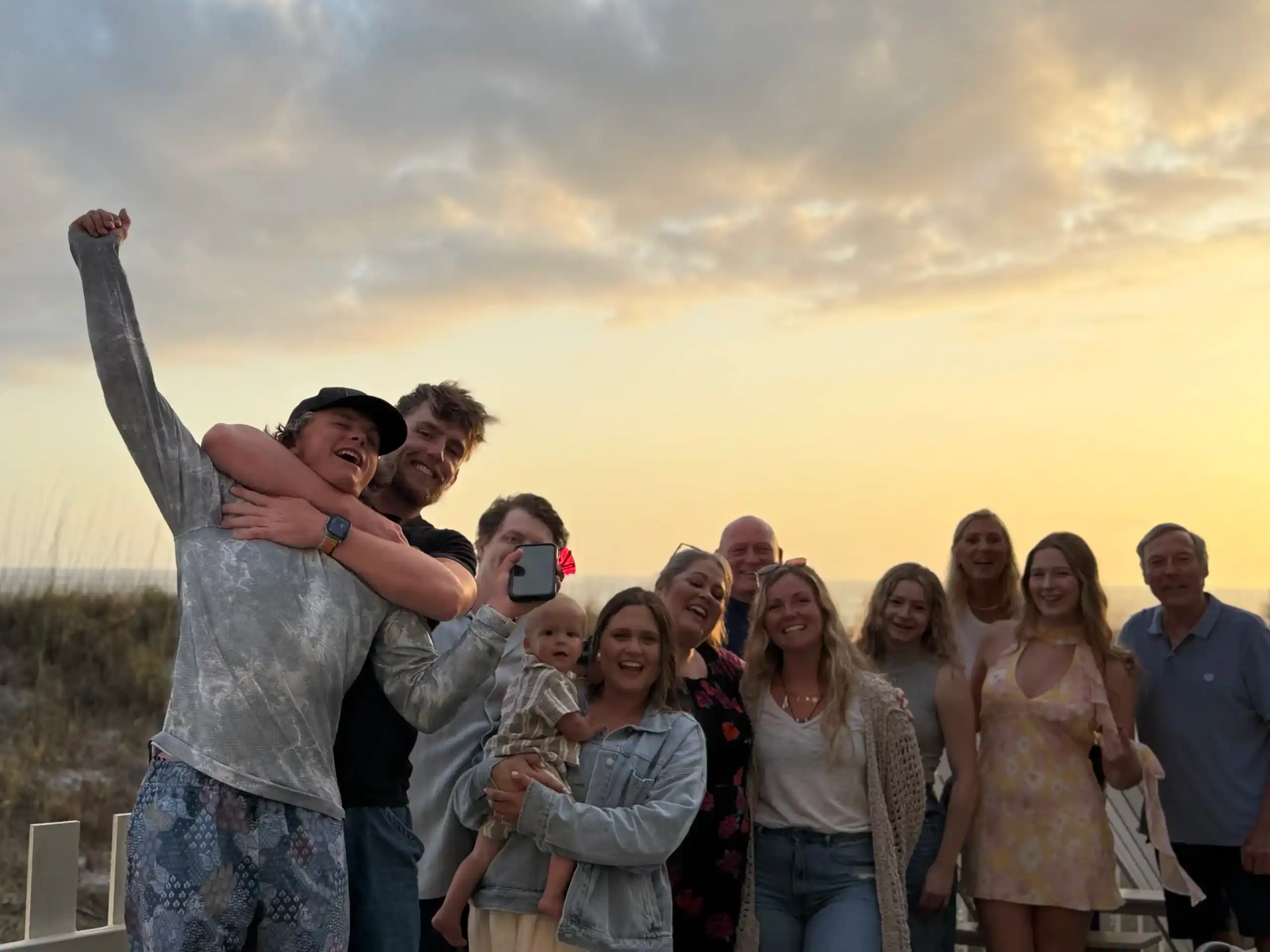 Group of friends and family smiling together at a beachside sunset birthday celebration in Florida